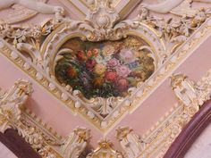 an ornate heart shaped painting on the side of a pink and white wall with gold trim