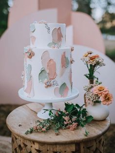 a white and pink cake sitting on top of a wooden table next to some flowers