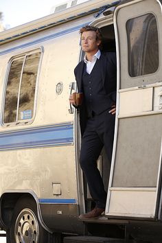 a man standing in the doorway of an old camper van, holding a drink