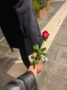 a person is holding a rose in their hand on the sidewalk with another person's foot