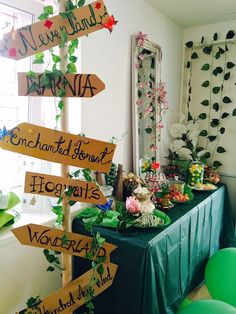 a table topped with lots of wooden signs next to a green chair and wall covered in greenery