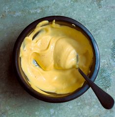 a bowl filled with yellow sauce on top of a counter next to a black spoon