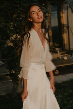 a woman in a white dress is standing outside with her hands on her hips and looking off to the side