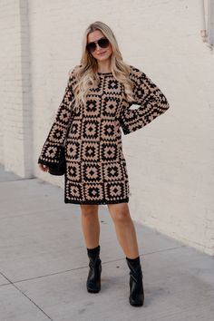 a woman standing on the sidewalk wearing a black and beige dress