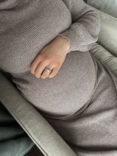 a pregnant woman laying on top of a couch with her hands under her stomach and wearing a ring