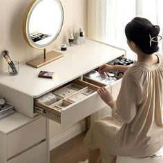 a woman sitting at a desk with drawers in front of her and looking into the mirror