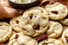 a pile of pecan cookies sitting on top of a wooden table next to a bowl of cream cheese