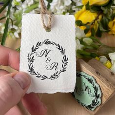 a hand holding a rubber stamp with the letter n and an initial on it next to flowers