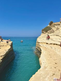 people are sitting on the edge of cliffs overlooking the ocean and boats in the water