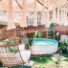 a bird cage sitting next to a small pool in the yard with chairs and umbrellas