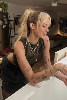 a woman sitting at a table with tattoos on her arms and arm, looking down