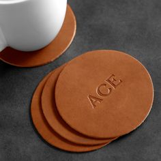 three coasters with the word aoe on them next to a coffee cup and saucer