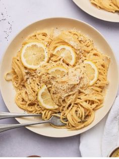 two plates of pasta with lemons and parmesan cheese on the side, next to silverware