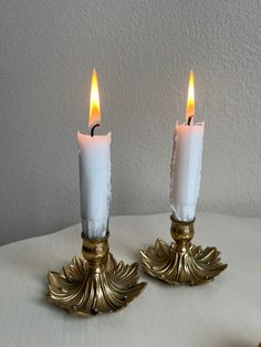 two white candles sitting on top of a table next to each other with one candle lit