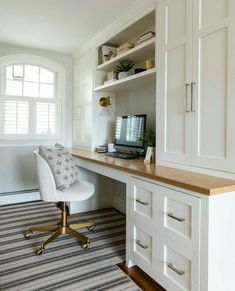 a desk with a computer on top of it in front of a white cabinet and window