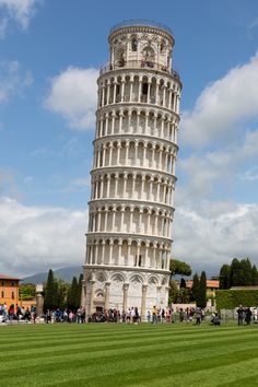 a very tall tower with people walking around in the grass near it on a sunny day