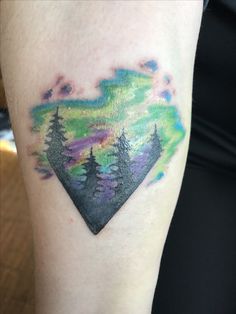 a colorful tattoo on the arm of a woman with trees and mountains in the background