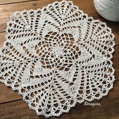 crocheted doily on wooden table next to ball of yarn