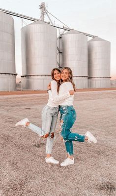 two girls hugging each other in front of silos