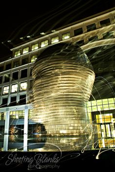 a building that is lit up at night with the lights on and reflecting off it's glass windows