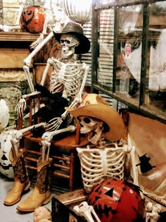 two skeletons sitting in chairs with pumpkins on the floor and other halloween decorations behind them