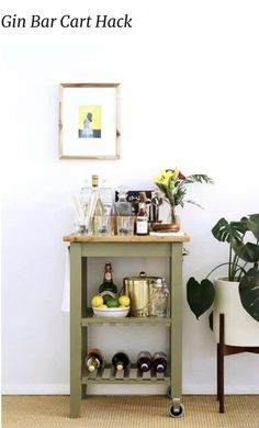 a small bar cart with bottles and glasses on it next to a potted plant