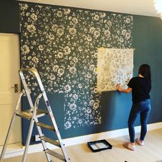 a woman is painting a wall with blue and white flowers