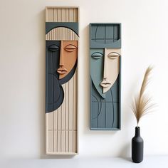 two wooden faces are on the wall next to a vase