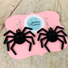 two black spider earrings on top of a pink piece of paper