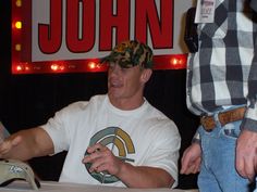 a man sitting at a table in front of a microphone and wearing a camo hat