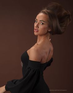 a woman in a black dress poses for a studio photo with her hair in a high bun