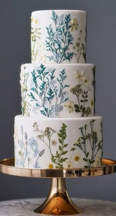 a three tiered cake decorated with flowers and leaves on a gold plated stand