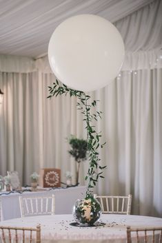 a balloon is attached to the top of a table at a wedding reception with greenery on it