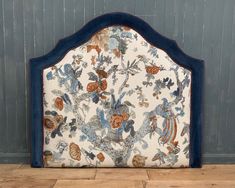 a blue and white headboard with an ornate design on the top, against a wooden floor