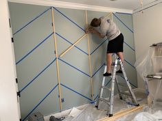 a man on a ladder painting the walls in a room that is being remodeled with blue tape