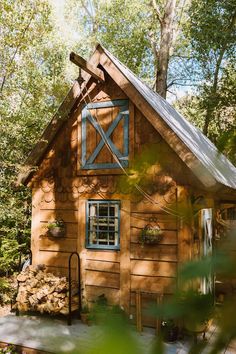 a small wooden building with a metal roof and window on the side, surrounded by trees