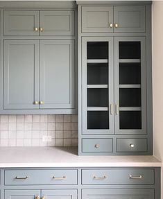 a kitchen with gray cabinets and white counter tops, gold pulls on the cupboards