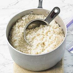 a pan filled with rice on top of a wooden board next to a measuring cup