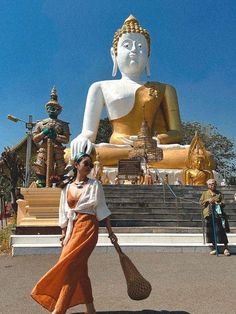 a woman is walking in front of a large buddha statue with a bag on her shoulder