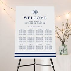 a welcome sign in front of a white wall with lights on it and a vase full of flowers