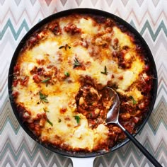 a skillet filled with meat and cheese on top of a cheesy table cloth