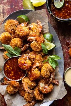 fried shrimp with dipping sauce and lime wedges on a plate next to other dishes