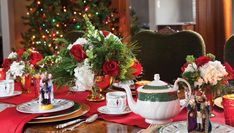 the table is set for christmas dinner with red and white flowers in teapots