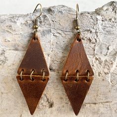 two brown leather earrings hanging from hooks on a rock