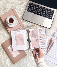 a person is writing in a notebook next to a laptop and cup of coffee on the floor