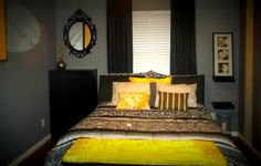 a bed with yellow and black pillows in a bedroom next to a window, framed pictures on the wall