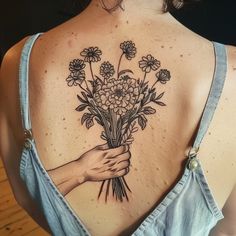 a woman's back tattoo with flowers on her shoulder and hand holding the bouquet