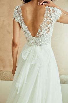 a woman wearing a wedding dress with a bow on the back and lace detailing at the neckline