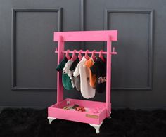 a pink toy rack with clothes hanging from it's hooks and two pairs of socks