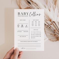 a person holding up a baby shower pass card with feathers around it on a table